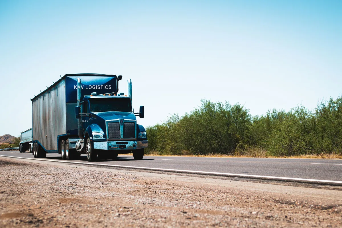 Blue KAV Logistics tractor pulling a trailer along a two-lane highway
