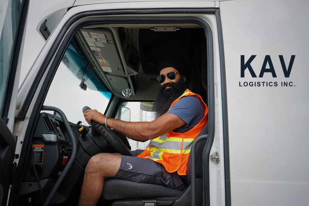 AZ truck driver in a safety vest at the wheel of a KAV Logistics truck
