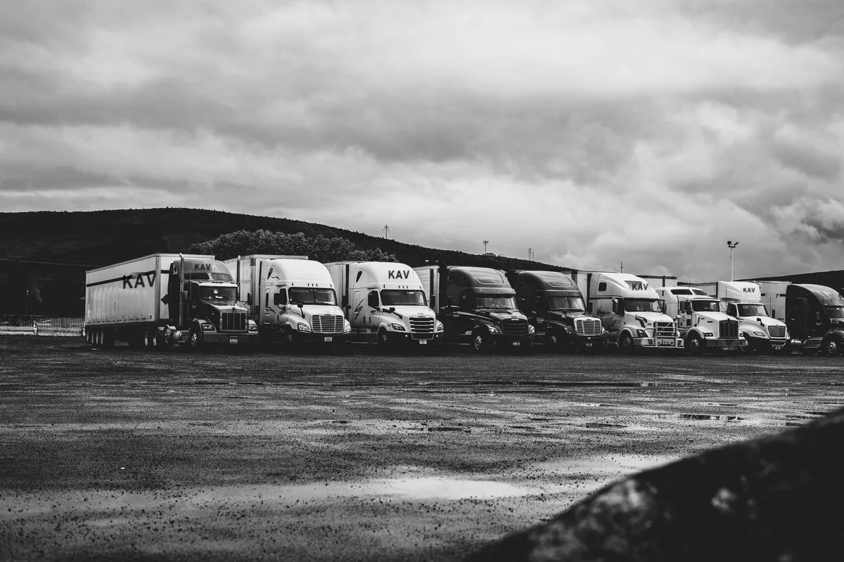 Row of KAV Logistics highway tractors and trailers parked in a truck yard