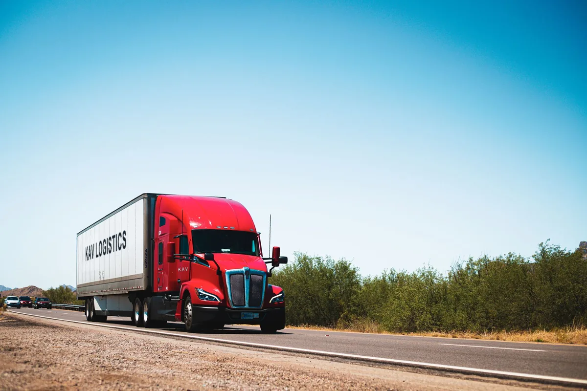Red highway tractor pulling a 53-foot KAV Logistics dry van trailer on an open highway