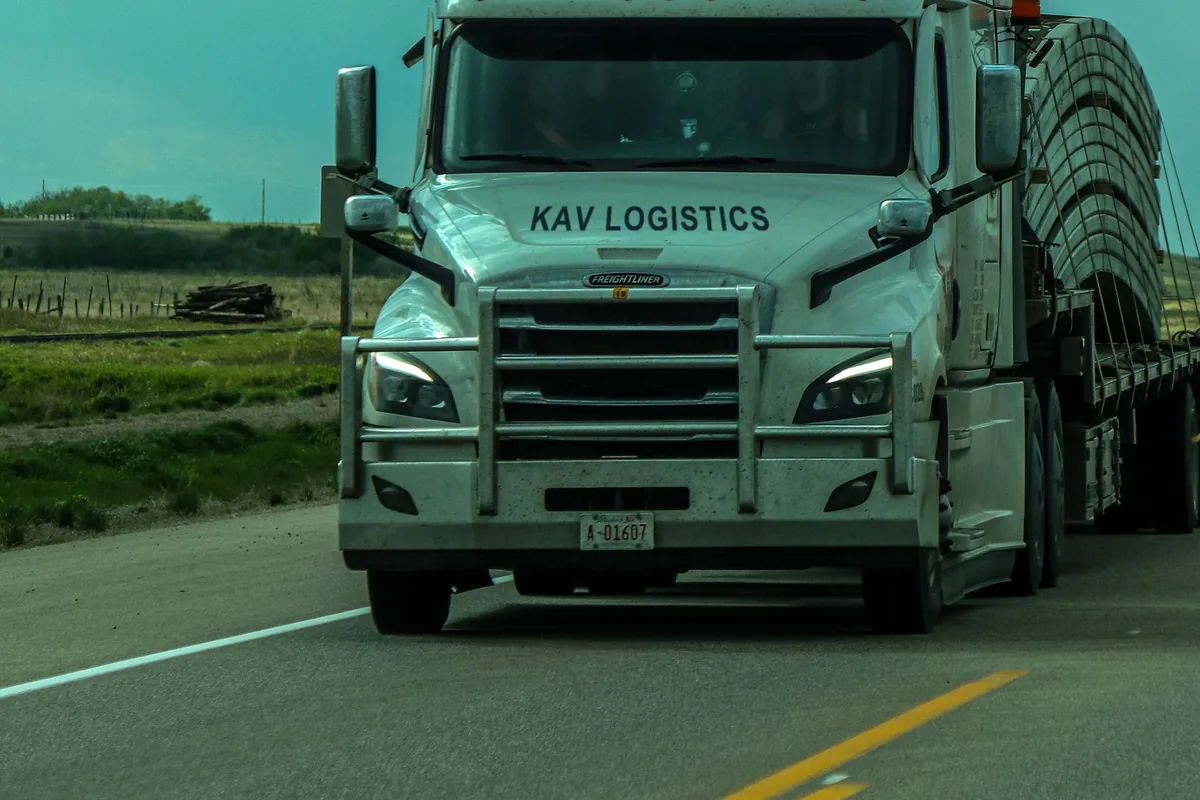 White KAV Logistics long-haul tractor on an open rural highway under a stormy sky